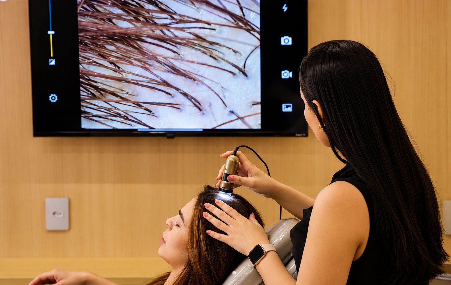 Dra. Ariela examinando o couro cabeludo com dermatoscópio digital, imagem ampliada na tela