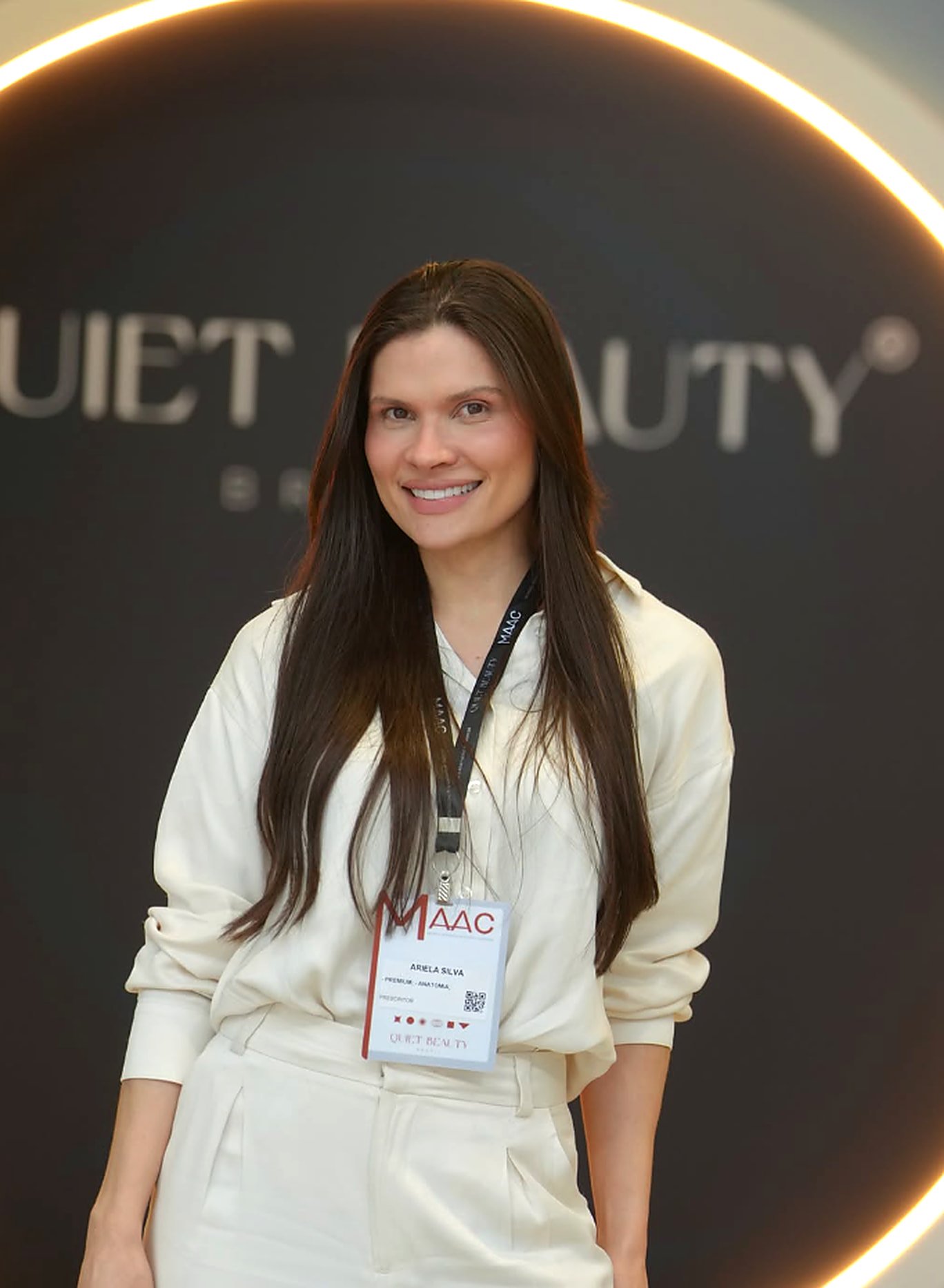 Dra. Ariela Santos de conjunto claro, sorrindo, no congresso MAAC 2026 em São Paulo